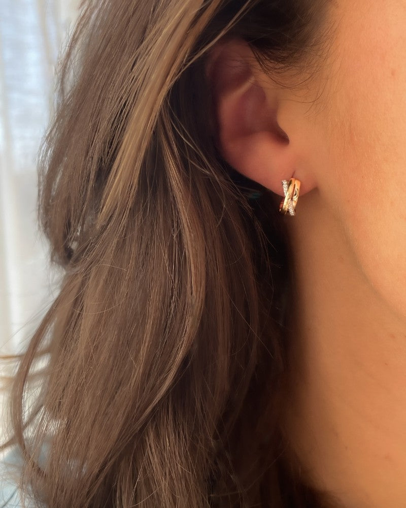 Close-up van het oor van een persoon met lang bruin haar, die Elegante Geelgouden Oorringen met Diamant van Excellent Jewelry draagt - subtiele 14 karaat gouden oorringen voor dames. De achtergrond is zacht vervaagd.
