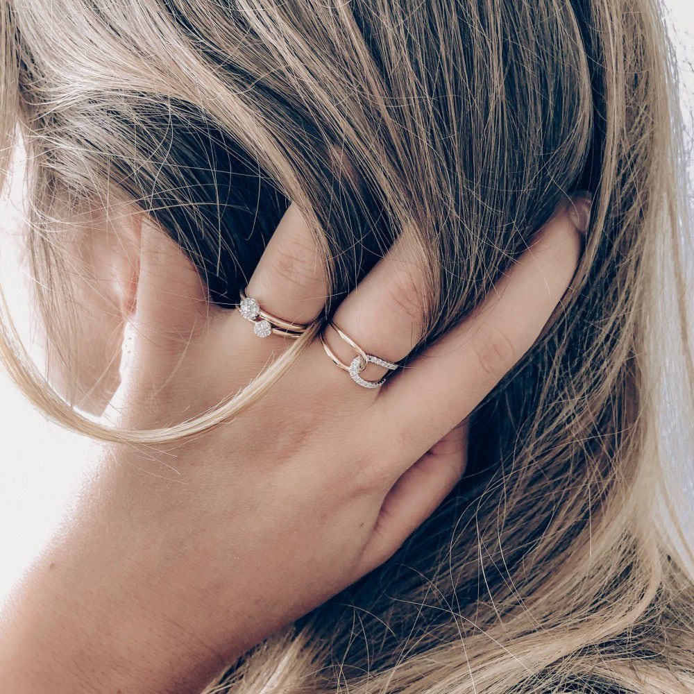 Een close-up van een blondine die haar hoofd aanraakt, met twee delicate 14K tweekleurige geel- en witgouden Excellent Jewelry damesringen met 0,18 ct briljant diamant aan haar vingers.