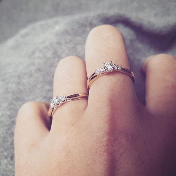 Een close-up van een hand met twee Excellent Jewelry Bicolor Geel- en Witgouden Ringen met Briljant 0.19 crt. aan de ring- en pinkvinger, tegen een zachtgrijze achtergrond.
