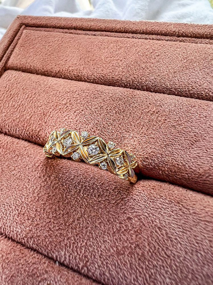 De Verfijnde Geelgouden Ring met Diamant - 0,19 crt van Excellent Jewelry, met een ingewikkeld geometrisch patroon en kleine diamantjes, wordt gepresenteerd op een zacht, roze fluwelen sieradenplateau.