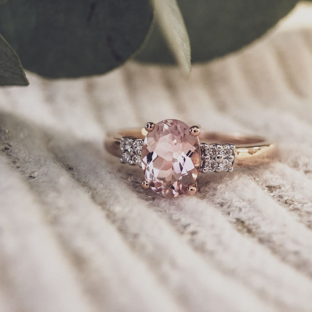 De 14 karaat roségouden ring met 1,03 ct morganiet en 0,07 ct briljanten van Excellent Jewelry ligt op crèmekleurige stof met groene blaadjes op de achtergrond.