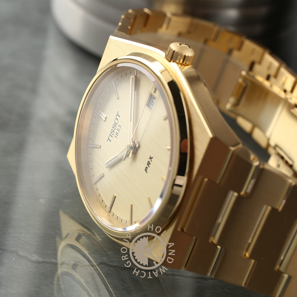 De Tissot PRX van Tissot wordt getoond op een reflecterend oppervlak, met een gouden afwerking, saffierglas, metalen band, minimalistische wijzerplaat en dagdatumvenster.