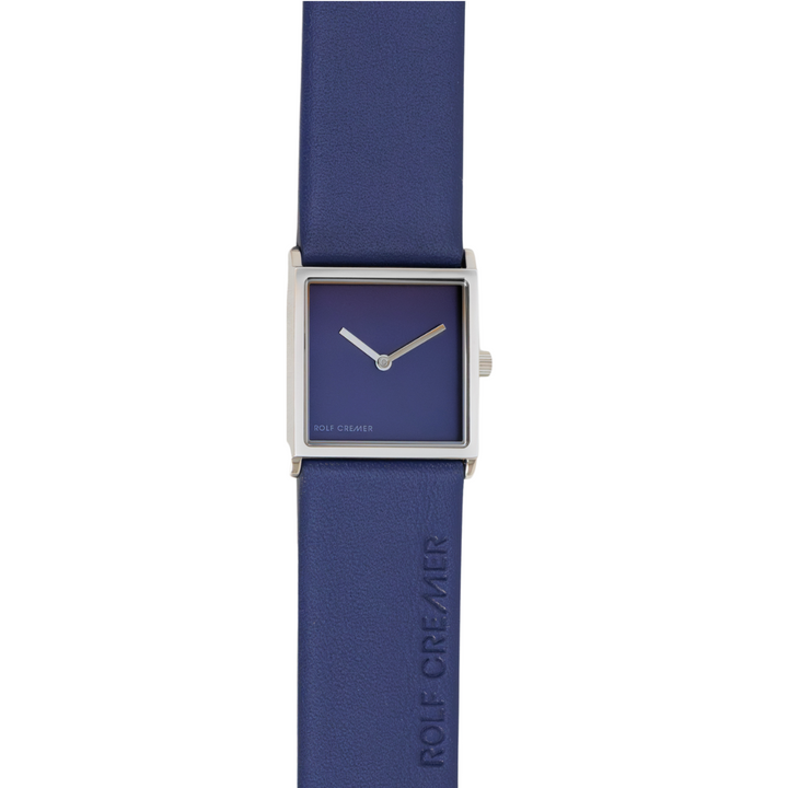 Het Rolf Cremer Horloge 508202 Groovy maakt deel uit van de Tidløs-collectie en heeft een vierkante zilveren kast met een blauwe wijzerplaat en twee zilveren wijzers. De blauwe leren band met reliëf ROLF CREMER en het quartz-uurwerk maken dit minimalistische, markervrije ontwerp compleet.