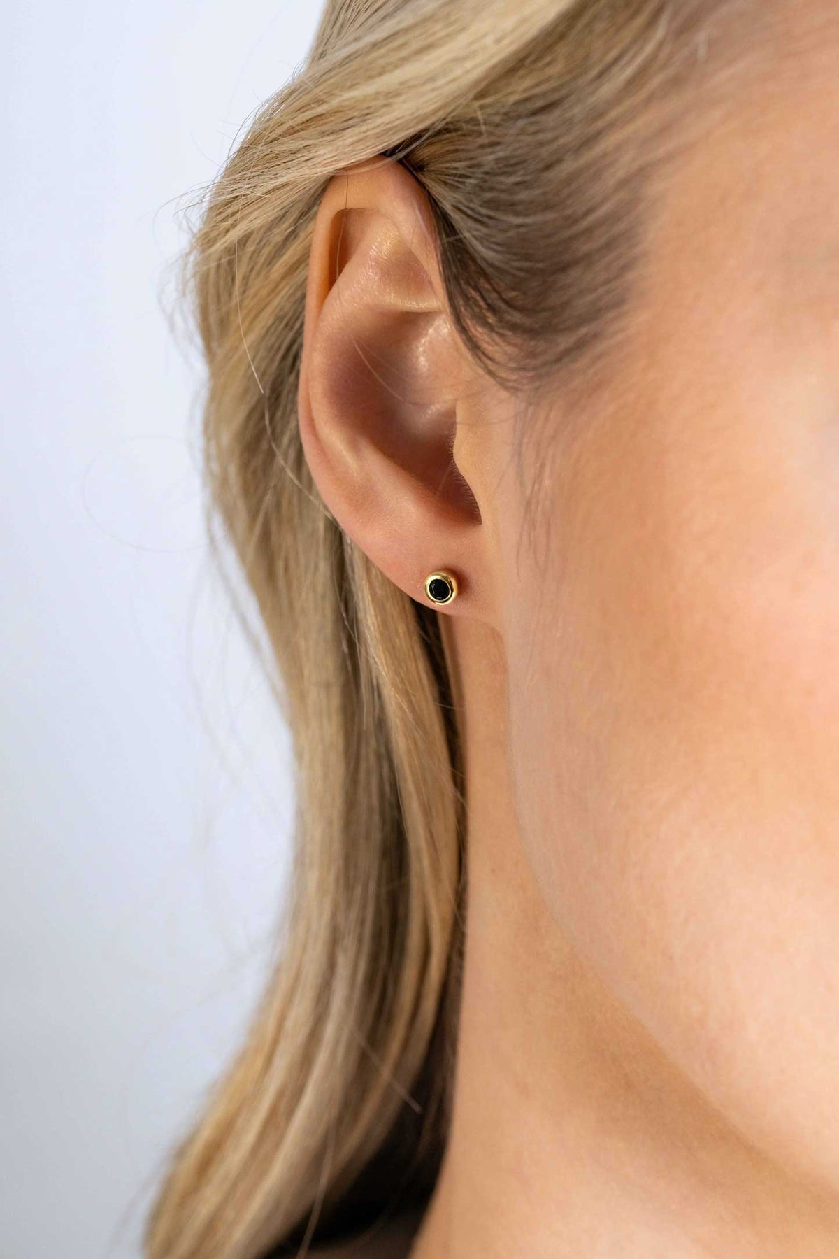 Boucles d'oreilles en plaqué or avec un design minimaliste et un détail central noir.
