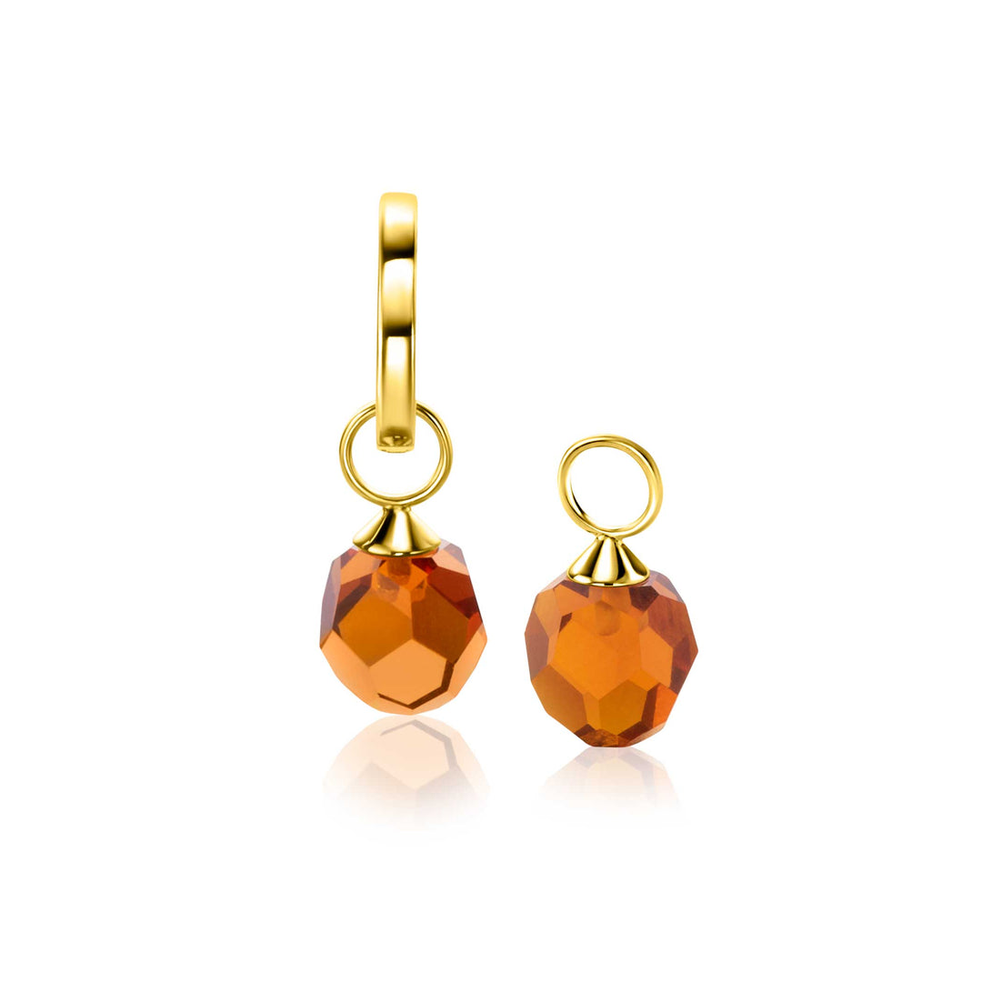Twee gefacetteerde oranje edelsteenbedels met gouden lussen voegen ZINZI elegantie toe. Eén wordt bevestigd aan een Zinzi Oorbellen Goud Zgch144 Br, als aanvulling op de traanvormige edelstenen. Hun reflecterende oppervlakken schitteren als stralende bruine kralen in het licht.