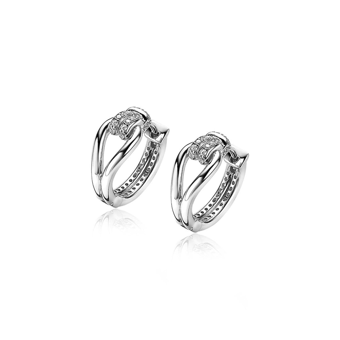 De Zilver Mvo19 oorbellen van Zinzi zijn zilveren creolen met een ingewikkeld ontwerp, versierd met kleine diamantaccenten en een gepolijste afwerking. Ze vormen een moderne en elegante stijl op een effen witte achtergrond.