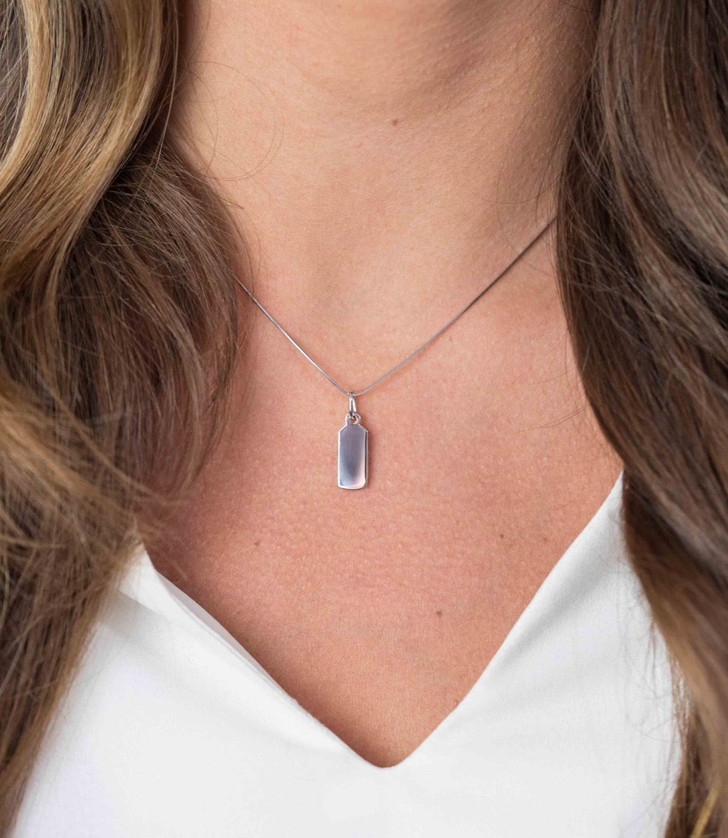 Pendentif en argent avec une forme rectangulaire, suspendu à une chaîne délicate.