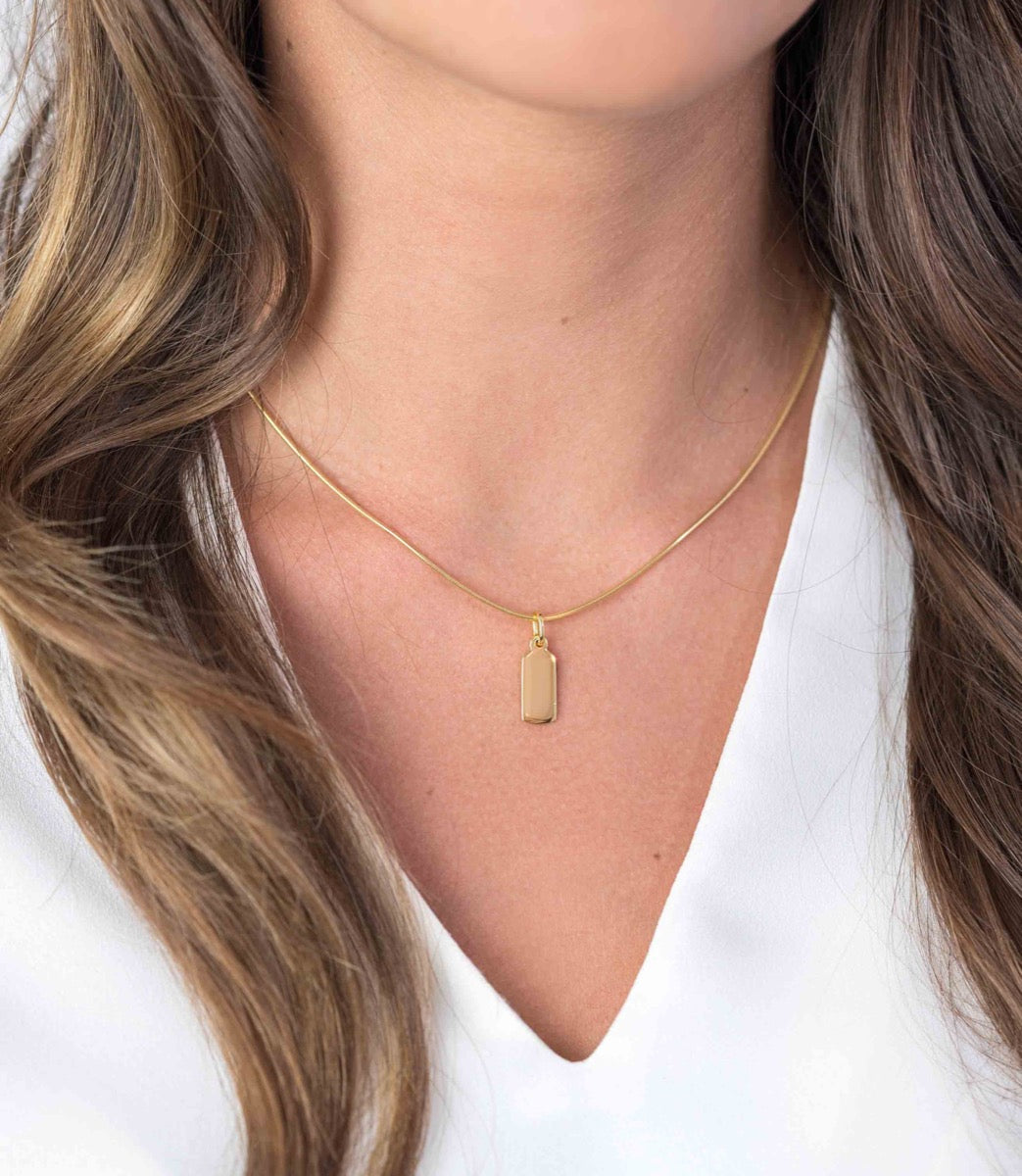 Pendentif doré en forme rectangulaire suspendu à une chaîne fine.
