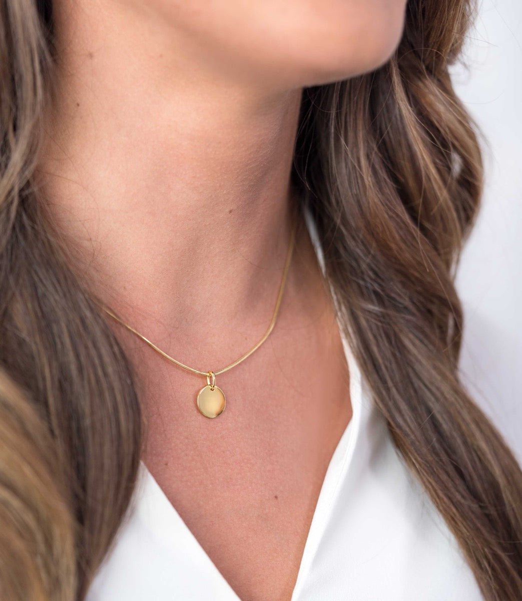 Pendentif doré en forme de disque suspendu à une chaîne fine.
